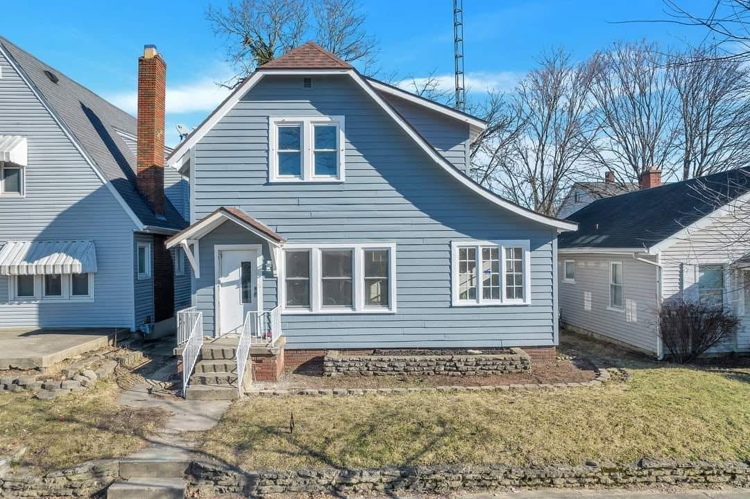 Blue and white two-story house with gabled roof, front porch, and bare trees, situated on a residential street with neighboring homes