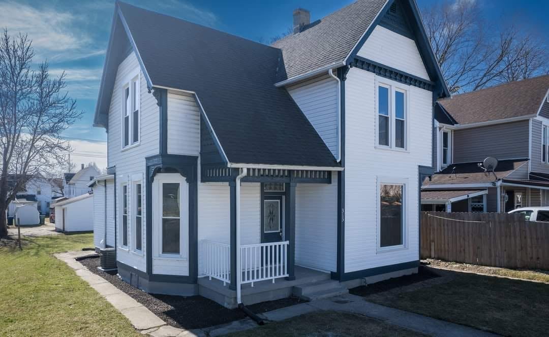 White and dark blue Victorian-style house with wraparound porch and manicured yard on a sunny day