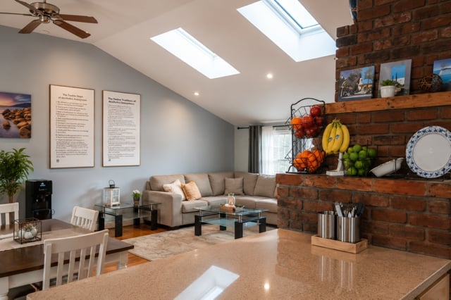 Modern living room with skylight, brick wall shelving, gray sectional sofa, and kitchen counter in foreground