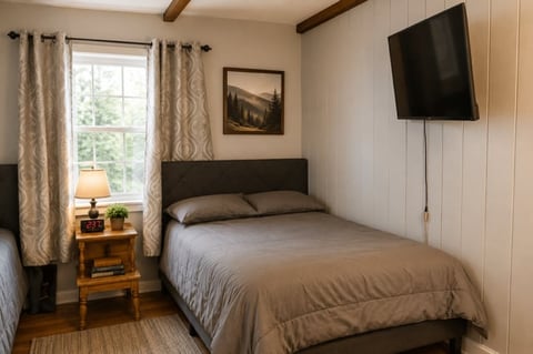 Cozy bedroom with a queen bed, wall-mounted TV, wooden nightstand, and window with patterned curtains