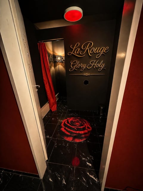 Interior of La Rouge Glory Hole adult establishment with red neon lighting, dark walls, and red rose floor design