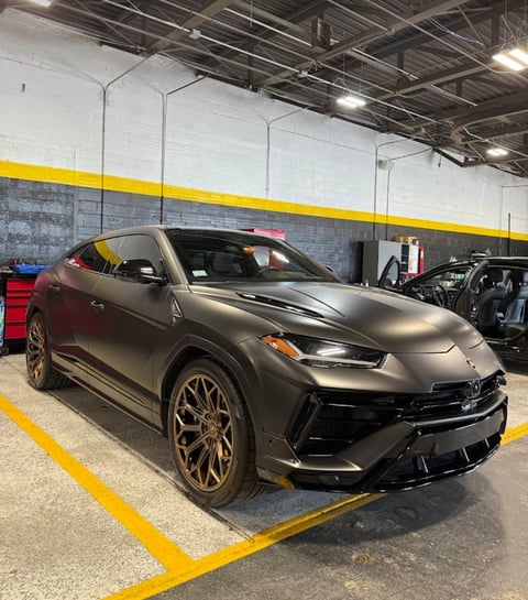Dark metallic Lamborghini Urus SUV parked in warehouse with yellow striped parking space markings