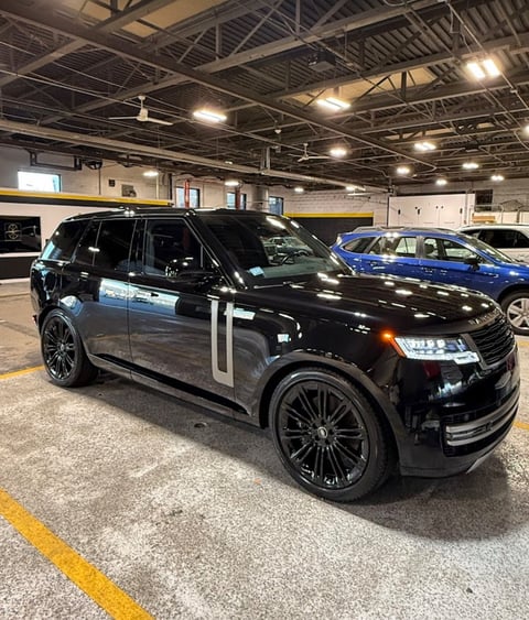 Black luxury SUV with custom wheels parked in indoor garage with other vehicles visible in background