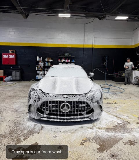 Gray sports car covered in white foam during a wash at an indoor detailing facility