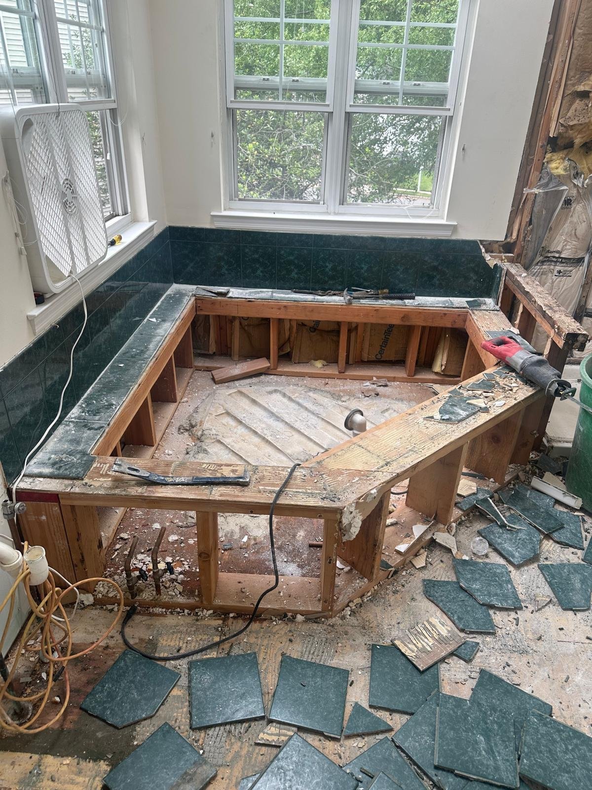 Wooden bench under renovation with removed cushions, sitting on a floor with torn carpet and tile in a bright room with windows