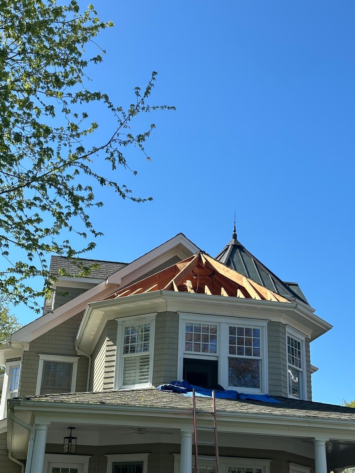 Victorian-style house with a distinctive octagonal cupola and turret under clear blue sky with tree branches visible at top left