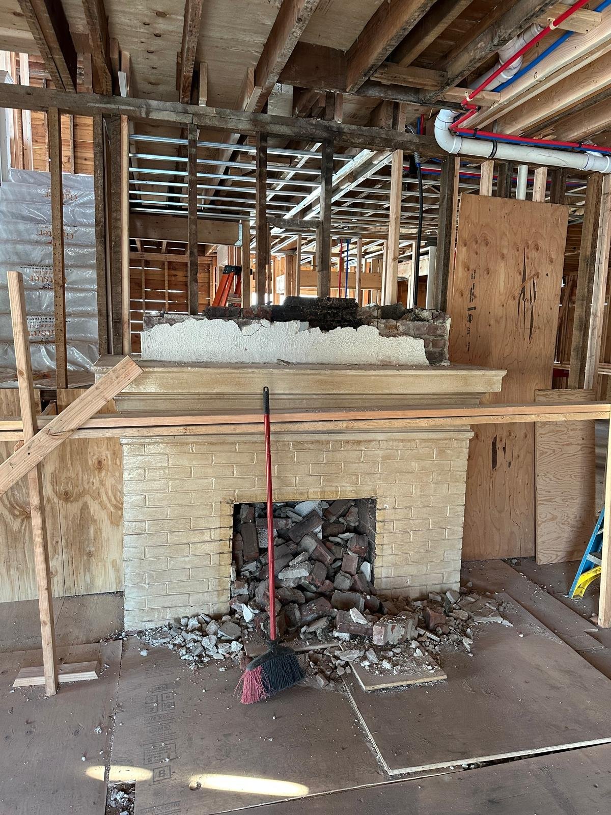 Interior of home under renovation showing brick fireplace with rubble, wooden framing, and demolition in progress