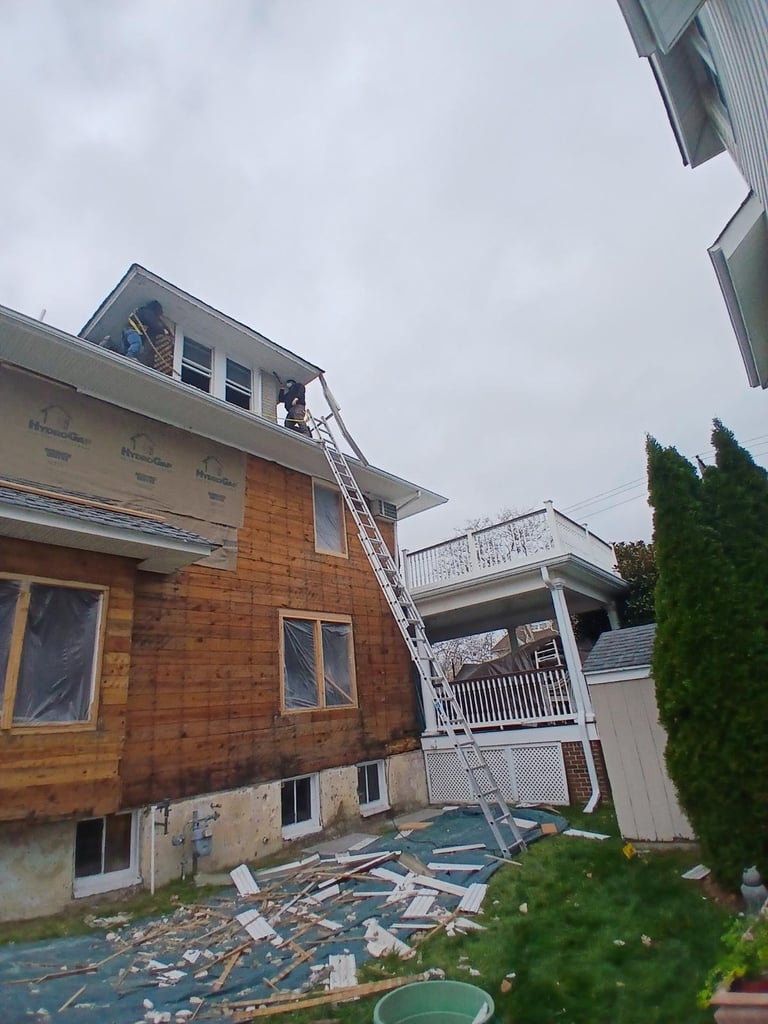 Construction workers on ladder against brick house under renovation with materials scattered below and overcast sky