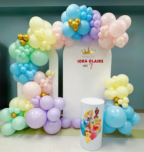 Colorful balloon garland backdrop with Princess Iora Claire banner, pastel balloons in pink, blue, purple, yellow, and green