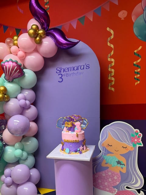 Shemaras 3rd birthday mermaid-themed party display with purple backdrop and tiered cake