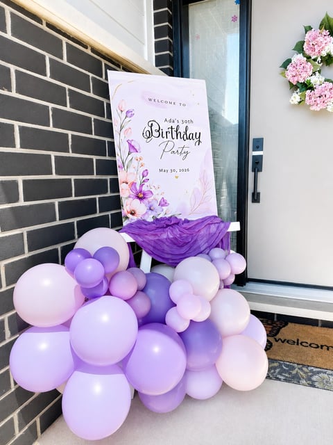 Birthday party entrance decorated with purple and pink balloons, floral welcome sign, and pink hydrangeas