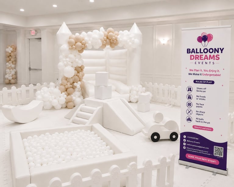 White and gold balloon arch display above a white ball pit and play structure in an indoor event space with Ballony Dreams Events signage