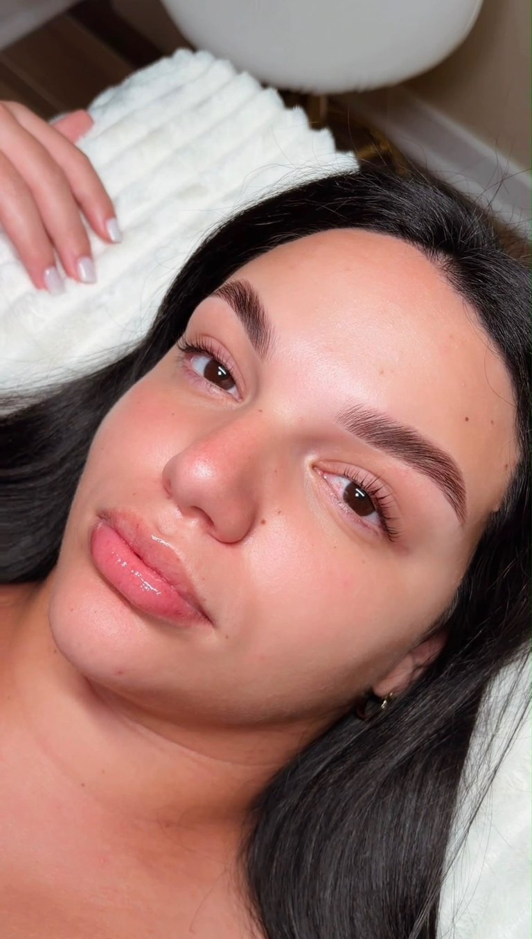 Close-up portrait of a woman with long black hair, natural makeup, pink lips, and a white towel wrapped around her head