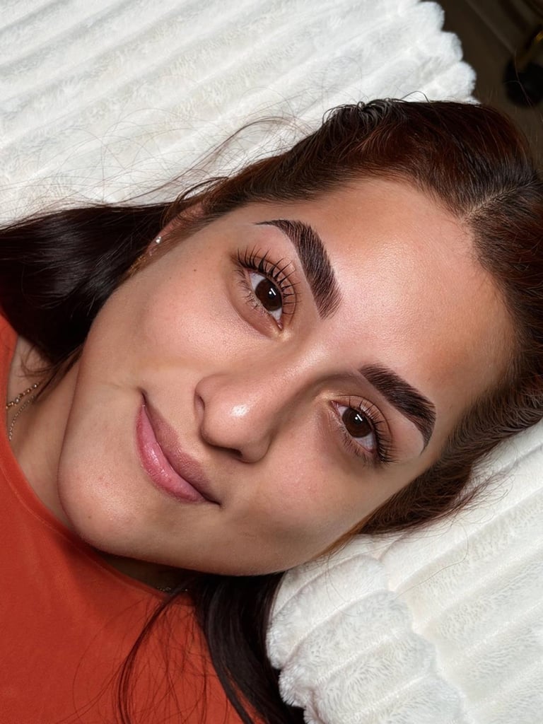 Close-up portrait of woman with dark hair and makeup wearing orange shirt, resting on white pillow