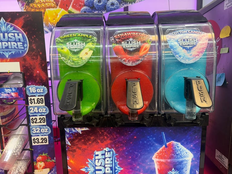 Slushie machine with three colorful dispensers: green apple, strawberry, and blue raspberry flavors with neon pricing display