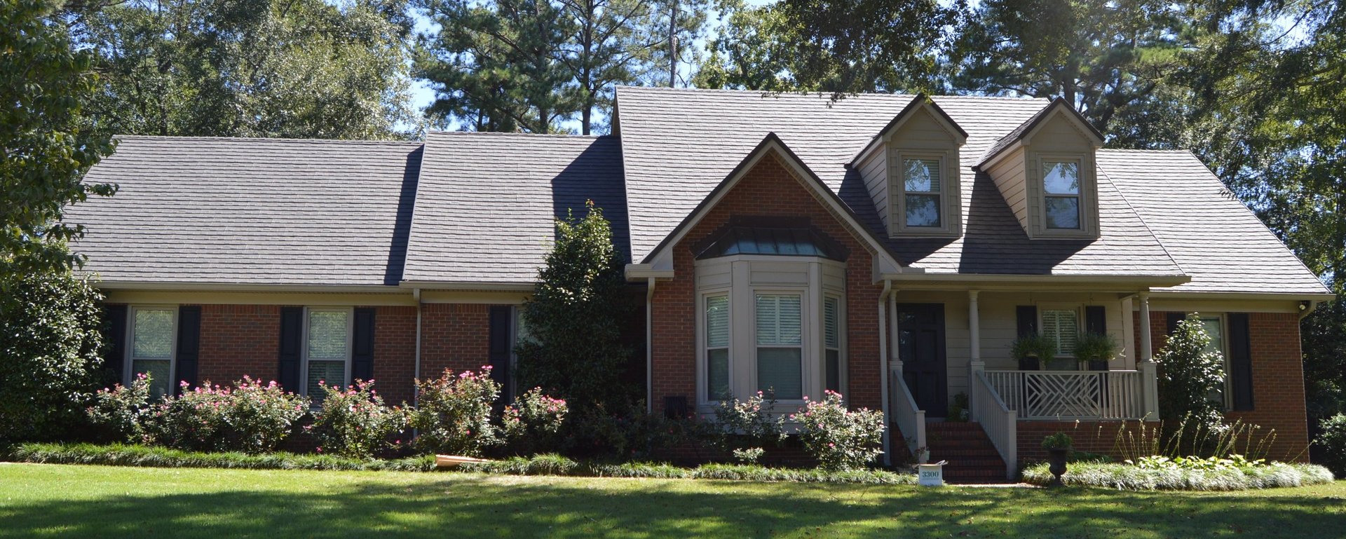 Two-story brick house with gray roof, front gable, and attached garage surrounded by green lawn and landscaping