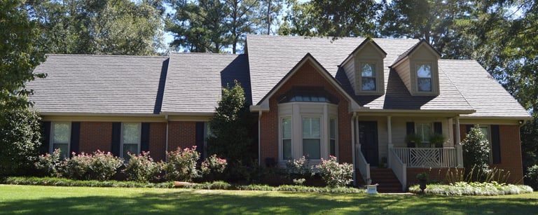 Brick two-story house with dormer windows, gray roof, front porch, and landscaped yard with green lawn and shrubs