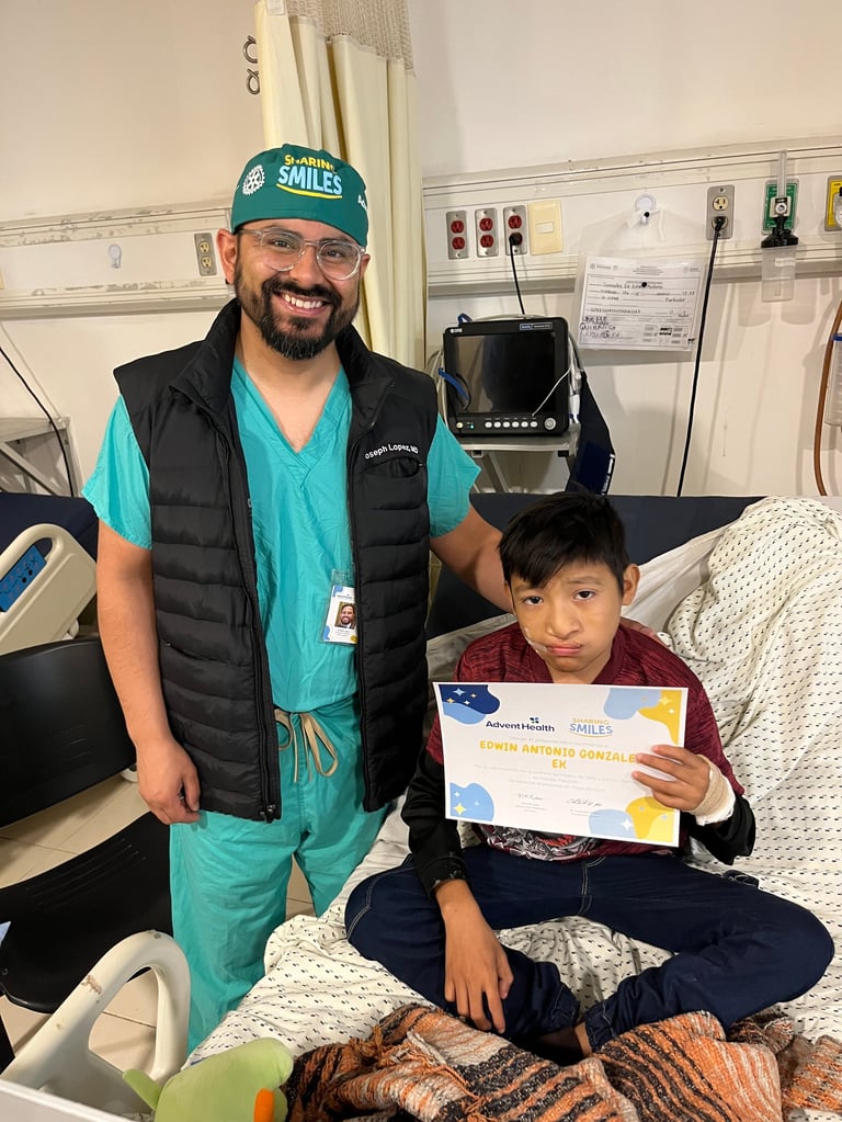 Médico con uniforme verde y gorro quirúrgico sonriendo junto a una niña que sostiene un certificado de participación