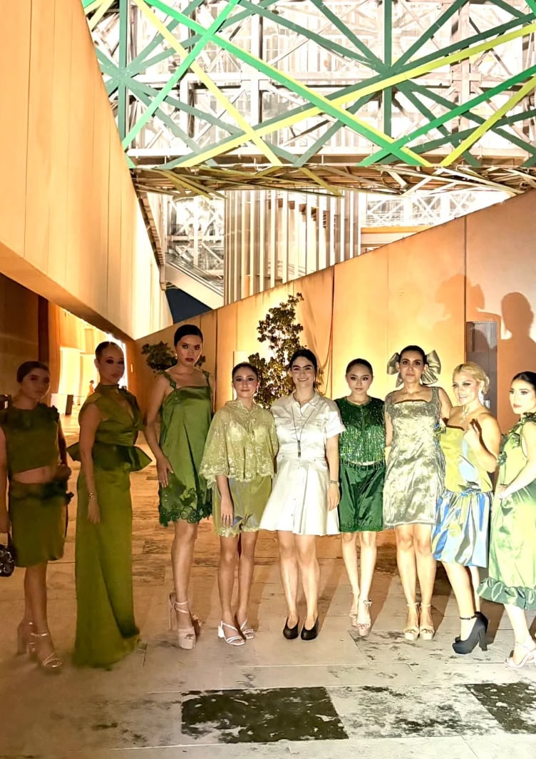 Fila de modelos en tonos verdes y neutros bajo una estructura industrial con vigas de colores, propuesta de Irene Liévanos Atelier