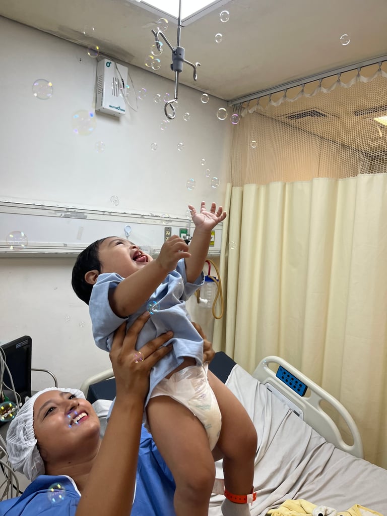 Adulto y niña jugando con burbujas de jabón en una habitación del hospital, ambos sonriendo