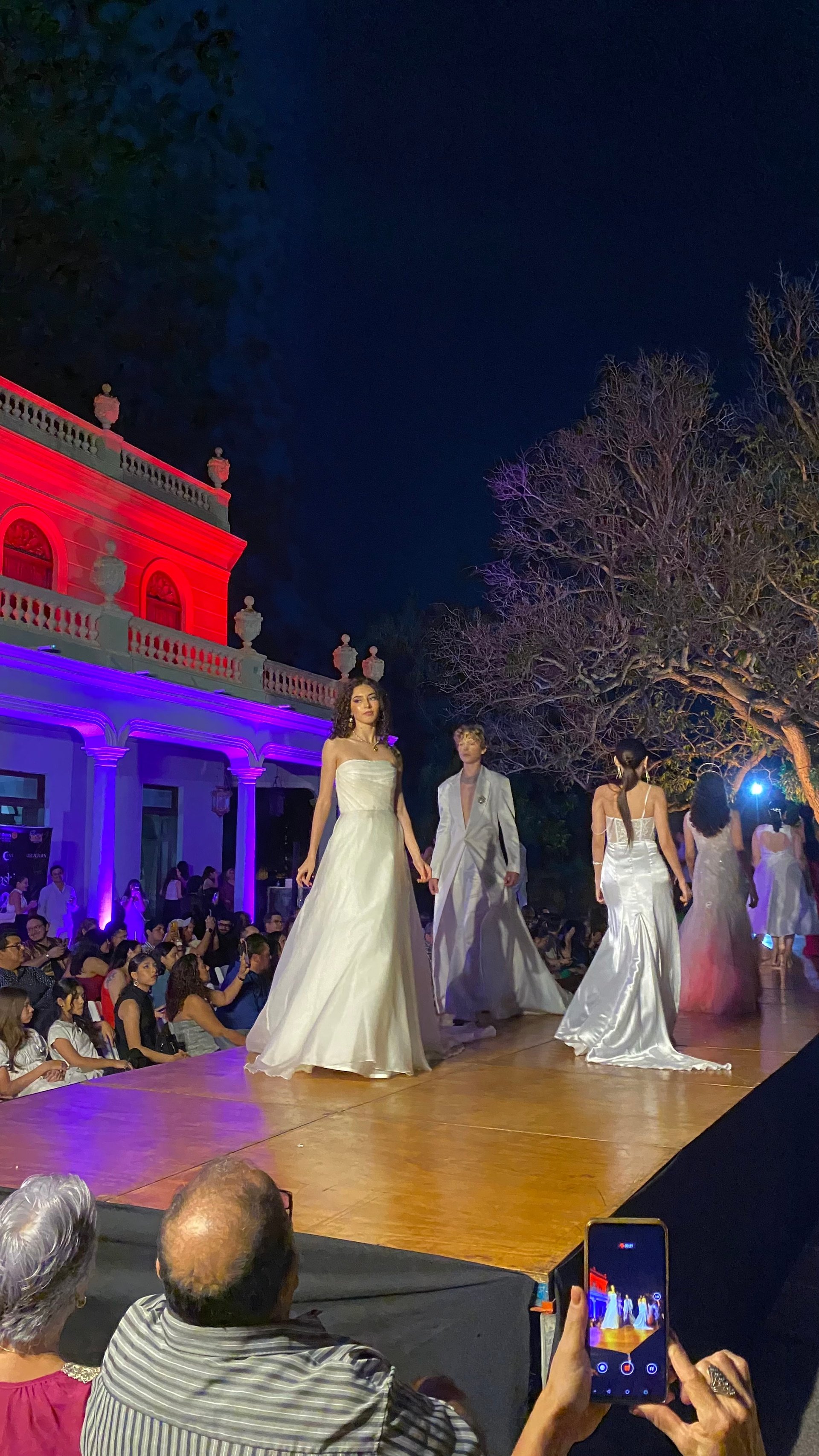 Modelos caminando en una pasarela nocturna al aire libre con un edificio clásico iluminado en morado de fondo