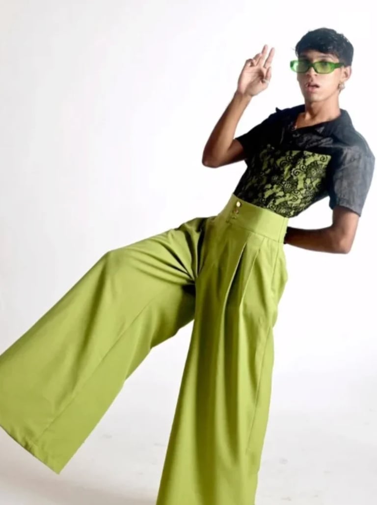 Joven modelo posando con lentes verdes, pantalón acampanado verde lima y playera gráfica oscura, propuesta de Leo Canché
