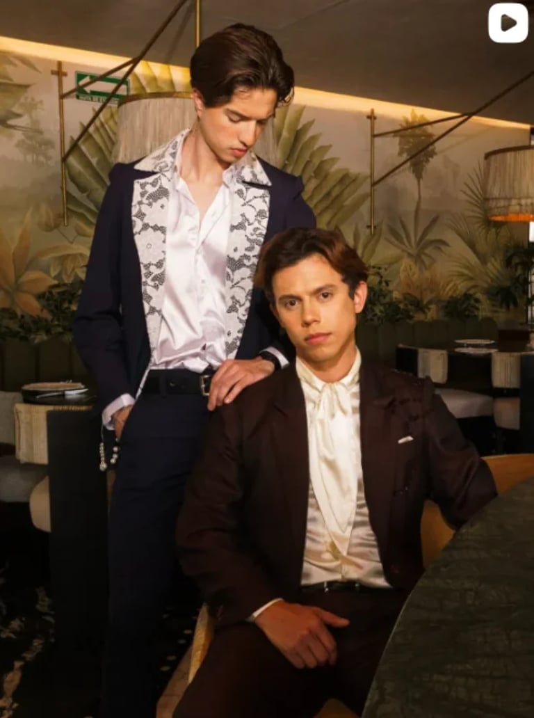 Dos jóvenes modelos con blazers formales y camisas blancas posando en un interior elegante con plantas tropicales, propuesta de Javier Baas