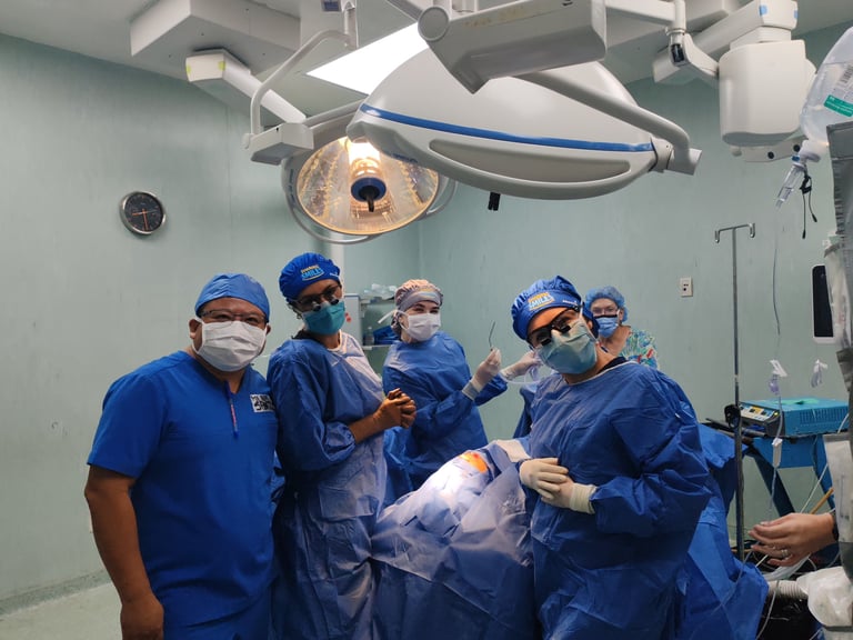 Equipo médico con uniforme azul y cubrebocas en quirófano bajo las luces de cirugía durante la jornada