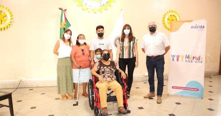 Grupo de seis personas de distintas estaturas posando frente a un muro decorado amarillo y blanco, una de ellas en silla de ruedas
