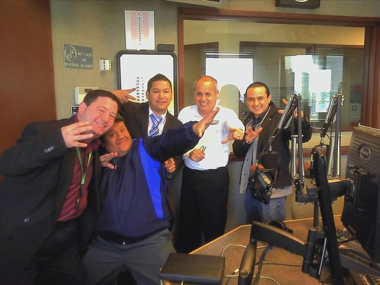Four men posing in a radio studio with microphone and equipment, making playful gestures at the camera