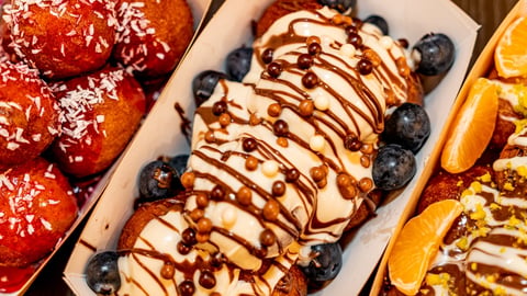 Overhead view of three colorful desserts: red glazed pastries, chocolate-drizzled cream with blueberries, and orange slice topped treats