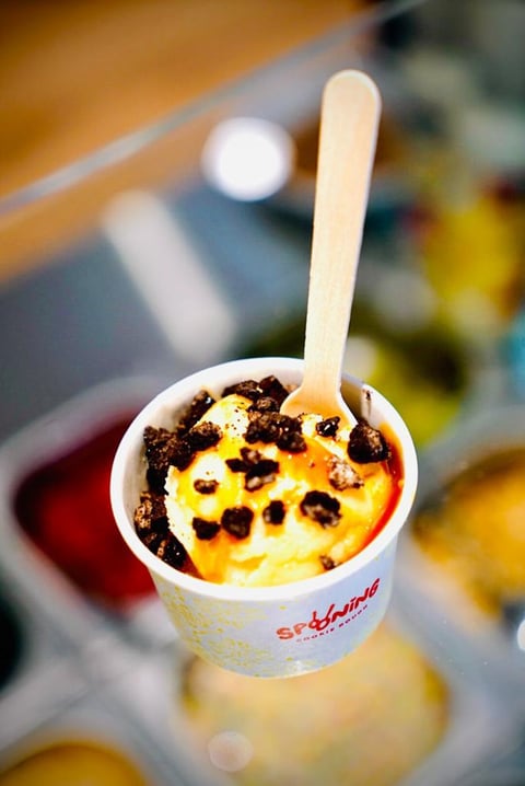 Cup of yellow ice cream topped with chocolate chips and a wooden spoon, on a wooden surface