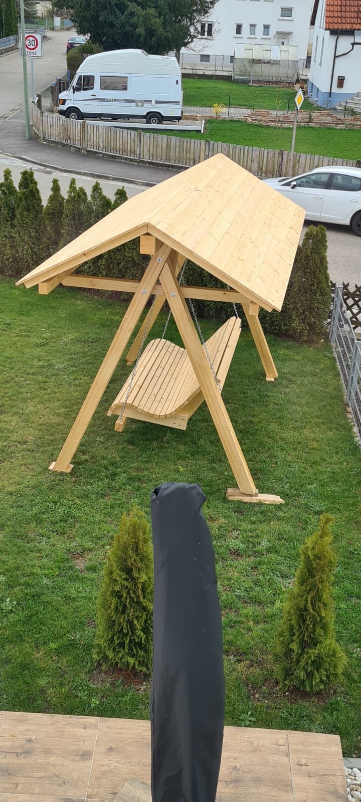 Wooden patio swing with A-frame design and pitched roof in a residential garden setting