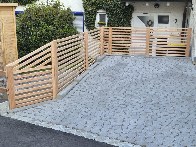 Modern wooden slatted fence with metal trim surrounding a paved driveway area outside a residential home
