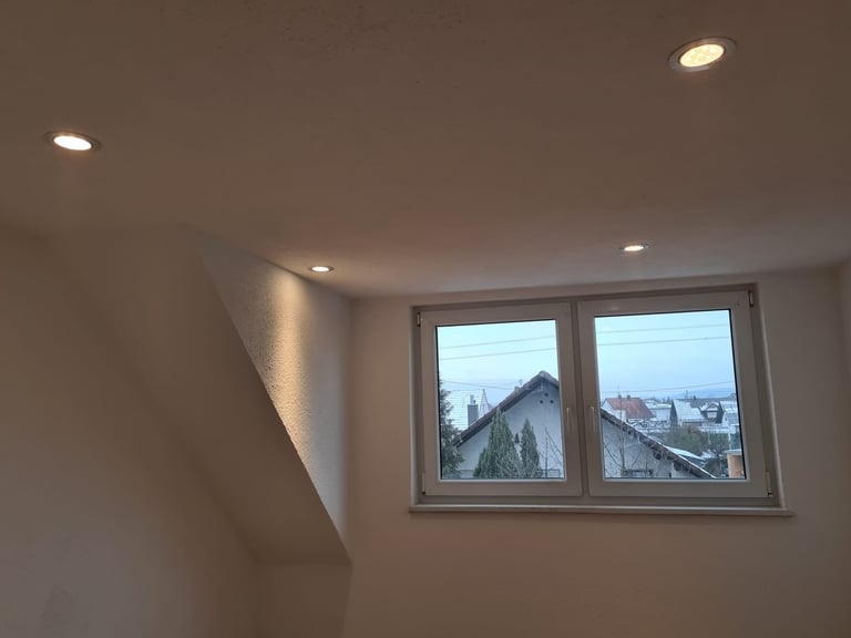 Interior room with white walls and recessed ceiling lights overlooking a snowy mountain landscape through a large double window