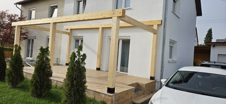 Wooden pergola attached to a white residential house with green plants and a parked white car visible