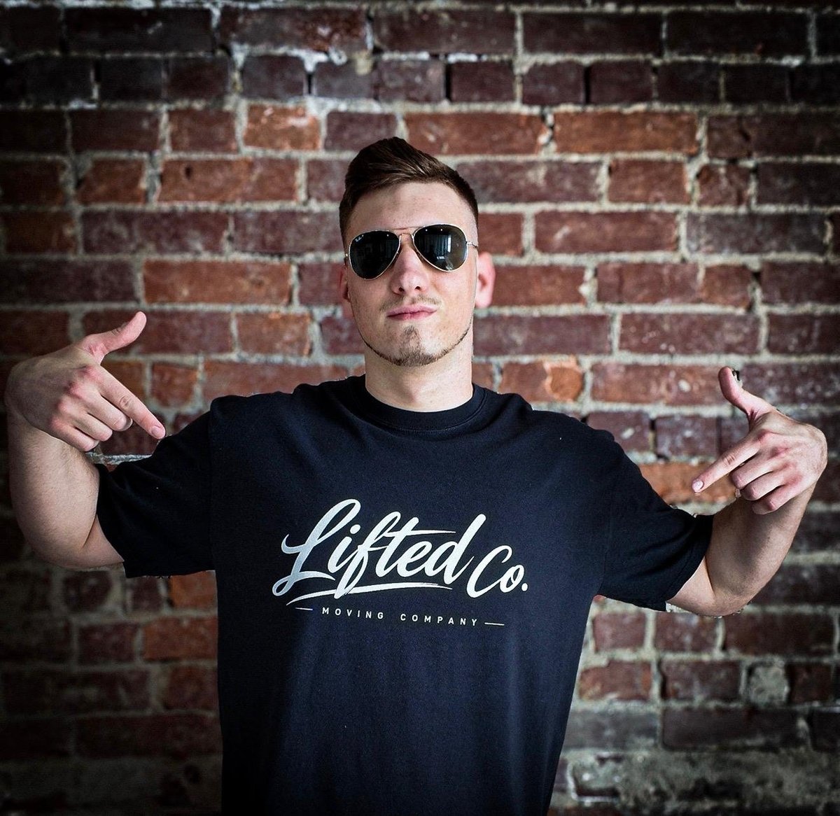 Lifted Co team member in a black Lifted Co. Moving Company t-shirt pointing at the brand logo