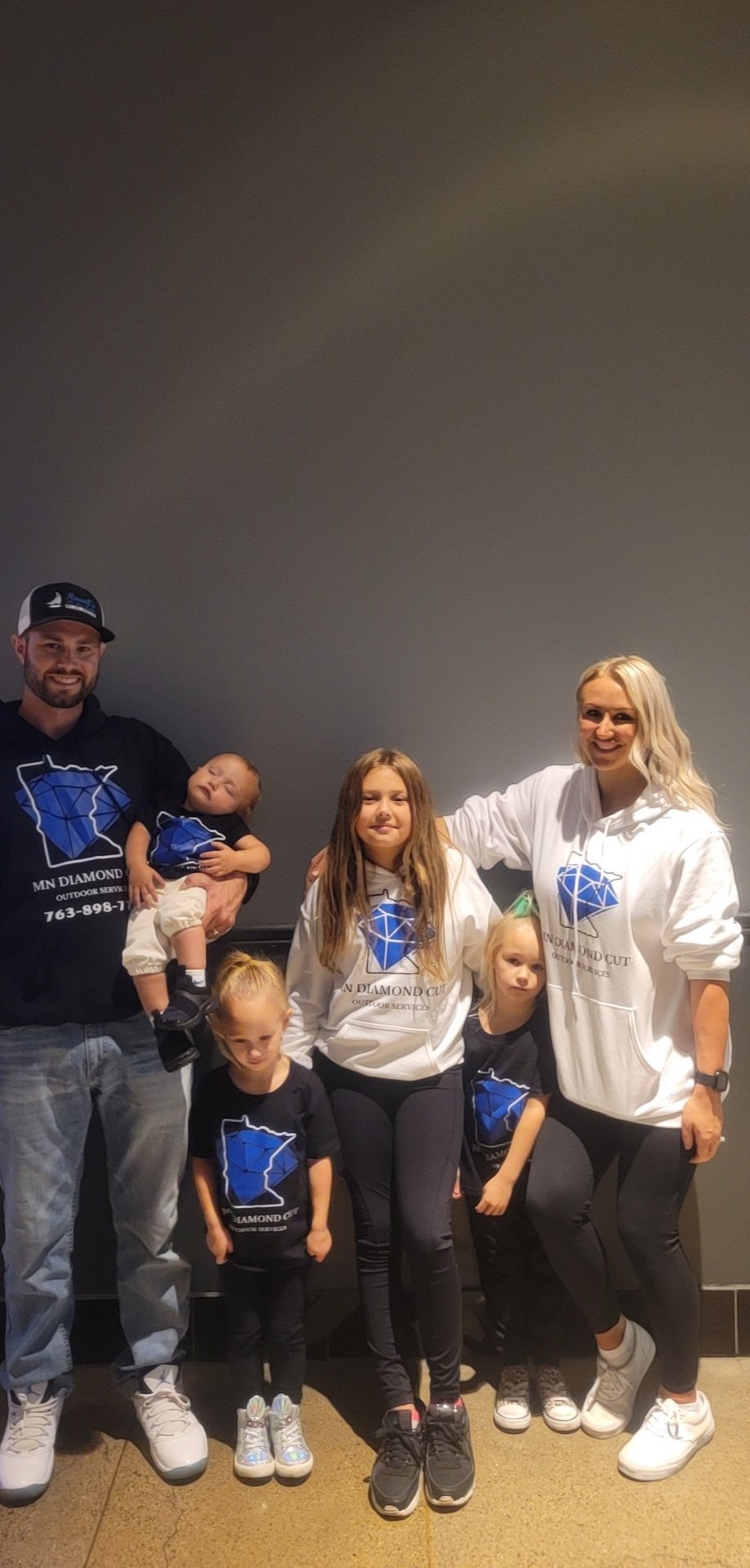 Family of five wearing matching blue Minnesota-themed shirts poses together against a gray wall