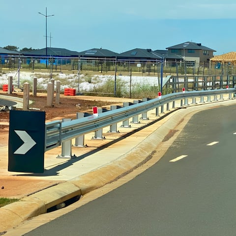 Construction site with metal guardrail, directional sign, and new residential buildings under development on cleared land