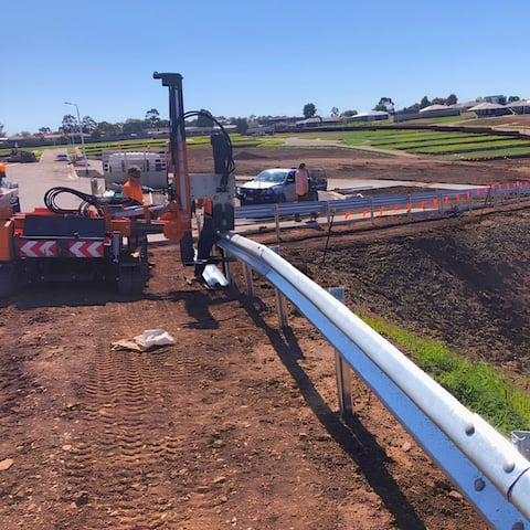 Orange construction machinery installing blue irrigation pipe in agricultural field with green crops and clear sky