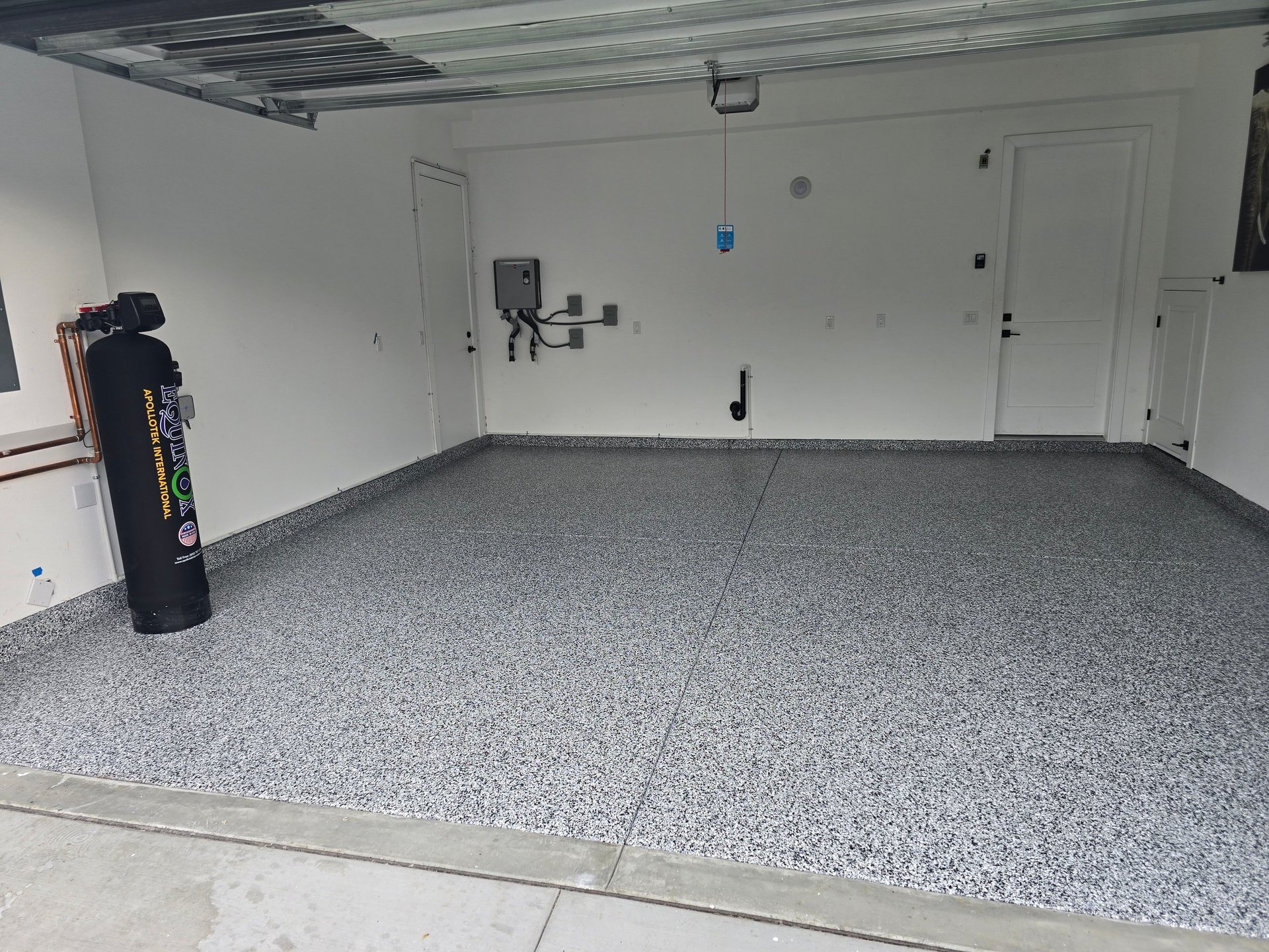 Empty garage interior with speckled gray epoxy floor, white walls, and overhead storage rack on ceiling