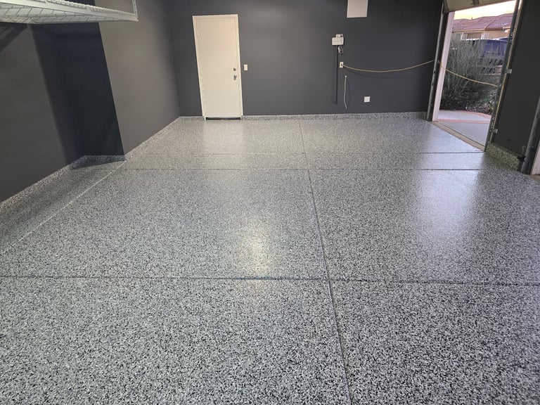 Empty garage interior with polished gray epoxy flooring, dark gray walls, and white door leading outside