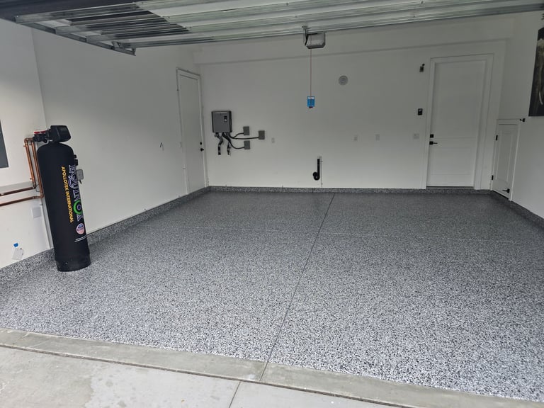Empty garage interior with gray speckled epoxy flooring, white walls, and a black trash can in the corner