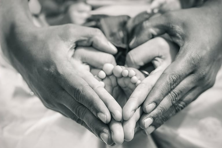 Manos de un adulto formando un corazón alrededor del pie de un bebé, fotografía en blanco y negro que evoca la conexión entre generaciones y los lazos familiares