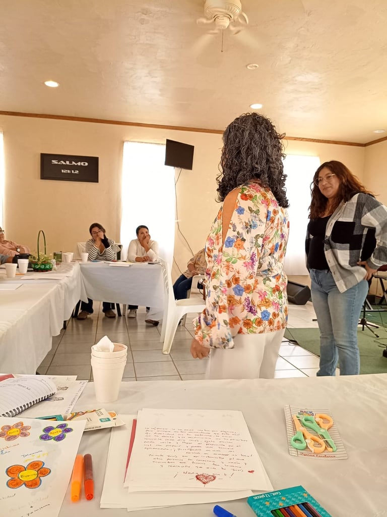 Mujer con cabello rizado y chaqueta floral hablando con otra mujer en un evento, con jueces sentados al fondo