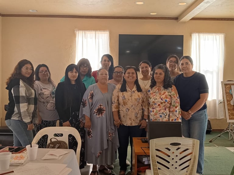 Grupo de mujeres posando juntas en una sala iluminada con ventanas, paredes beige y sillas blancas