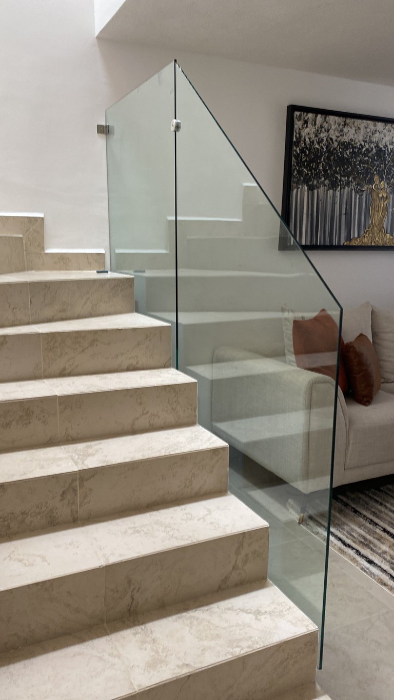 Modern staircase with beige marble steps and glass railing leading upward in a bright interior space
