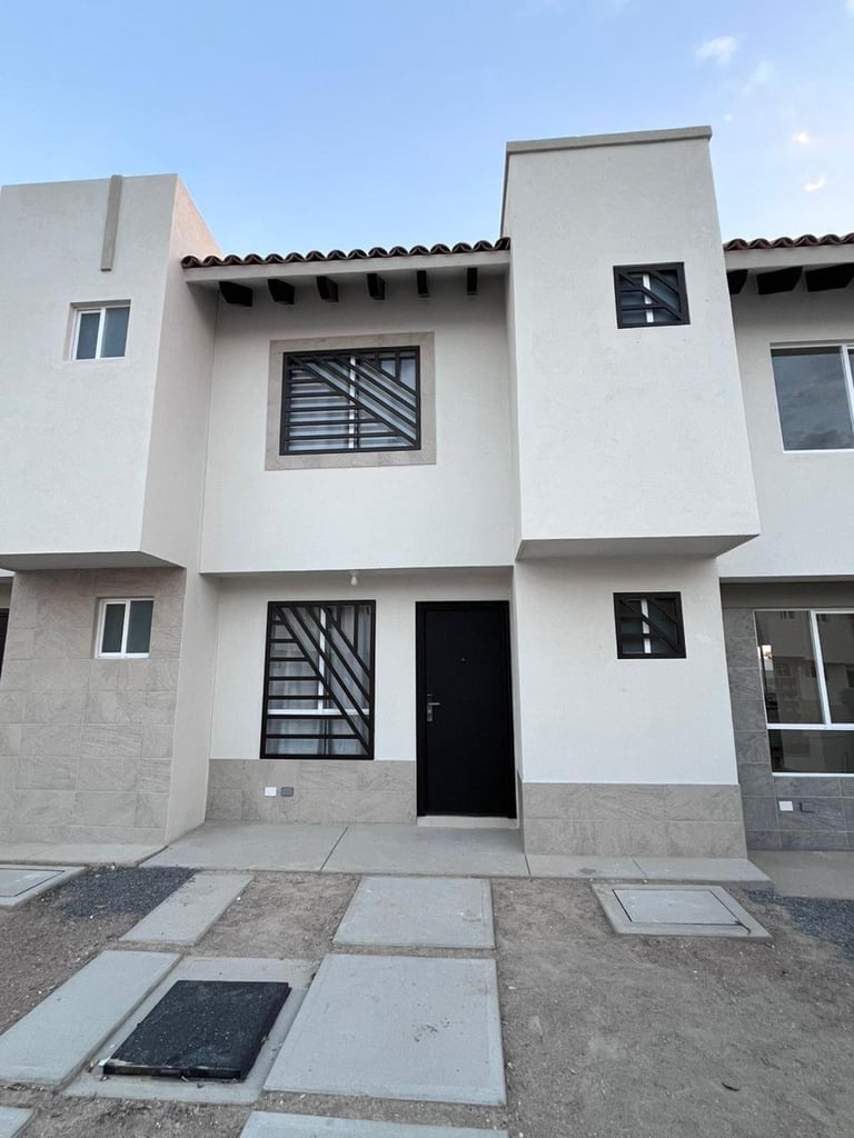 Modern white residential townhouse with black door and window grilles, concrete paving, and clear blue sky