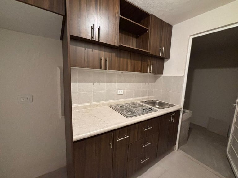 Modern kitchenette with dark wood cabinetry, white countertop, gas cooktop, and white subway tile backsplash