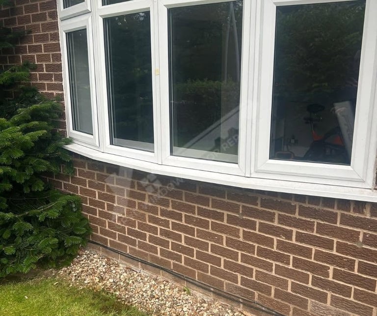 Bay window with white frames on red brick house exterior with gravel and green shrub